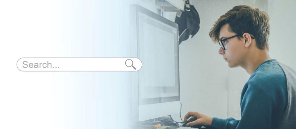 Teenager wearing glasses focused on a desktop computer, with a large search bar graphic on the left